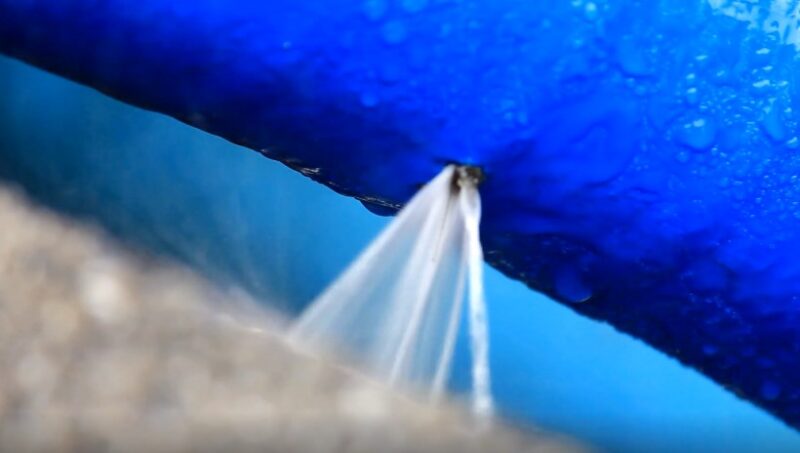 A leak in a blue pipe, water spurting out