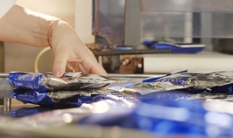 A close-up view of a worker carefully placing packaged goods onto a conveyor belt