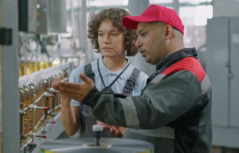 Two colleagues collaborate on a bottling line, reviewing the process