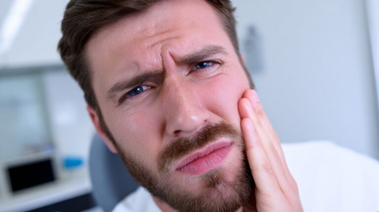 Man holding his cheek with a pained expression, suggesting severe tooth or jaw discomfort