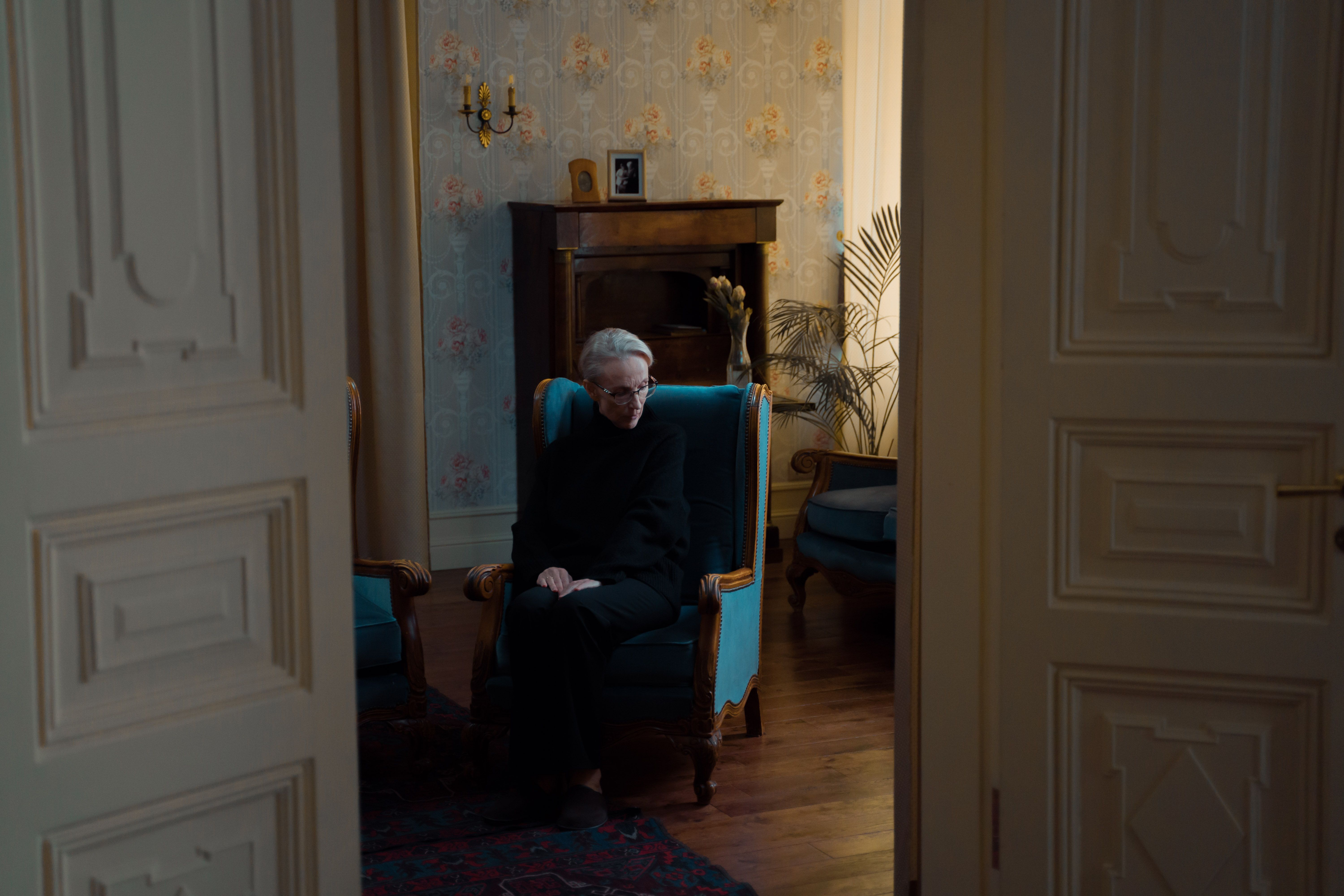 Elderly woman sitting alone in a dimly lit room, conveying isolation and solitude