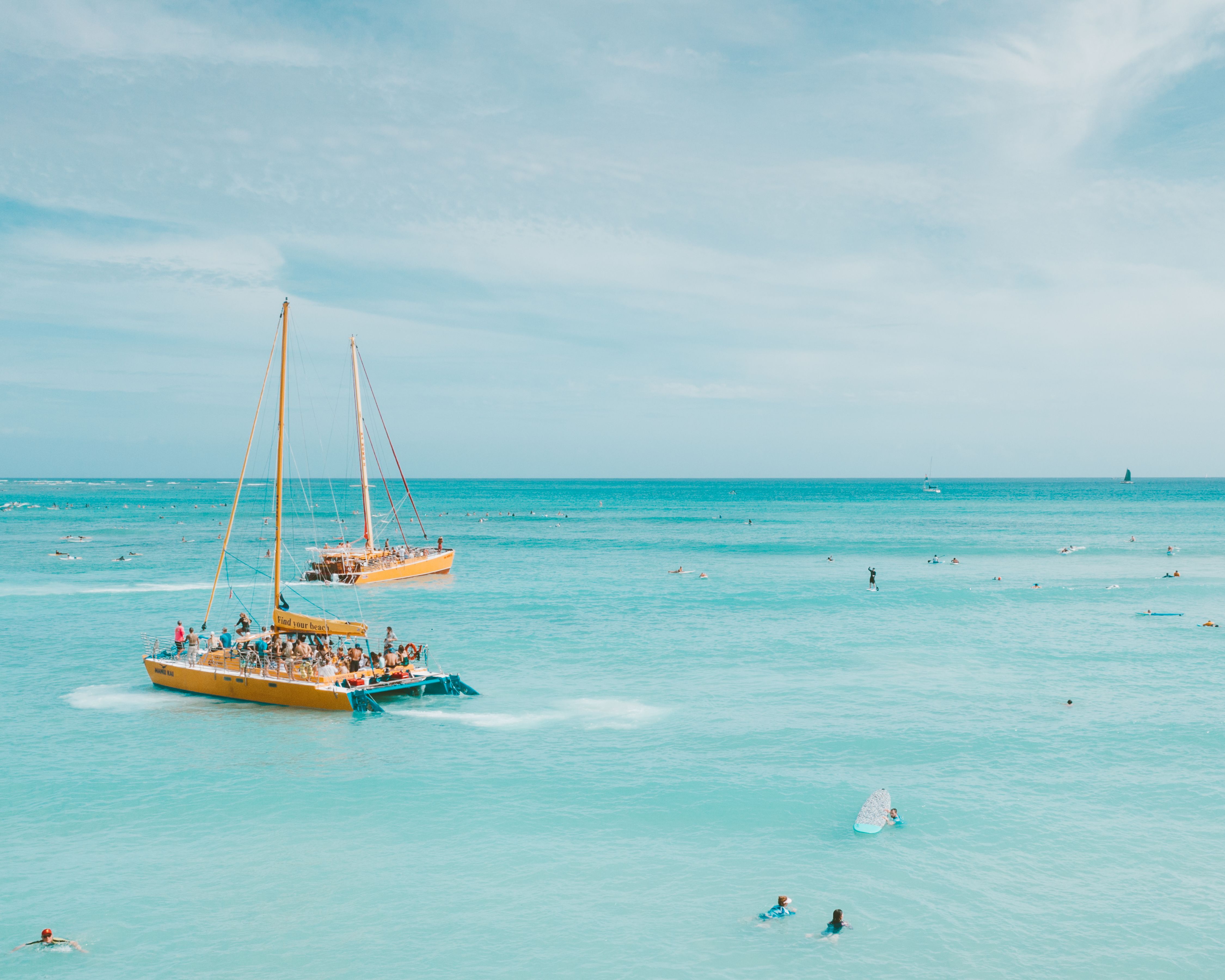 Two catamarans sail on turquoise Hawaiian waters, illustrating a shared group boat-tour experience.