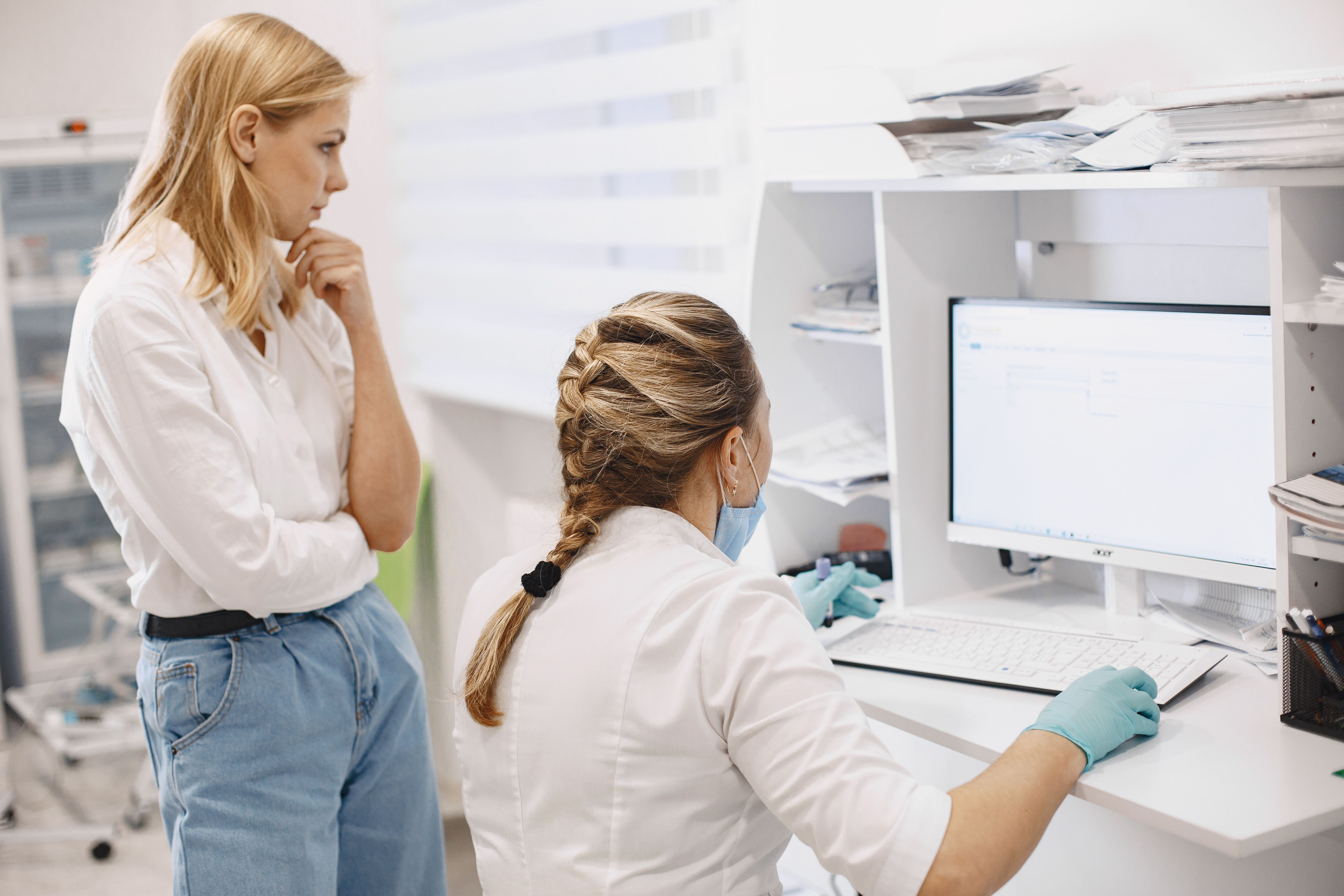 Two female healthcare workers collaborate in a clinic, analyzing data on a computer screen
